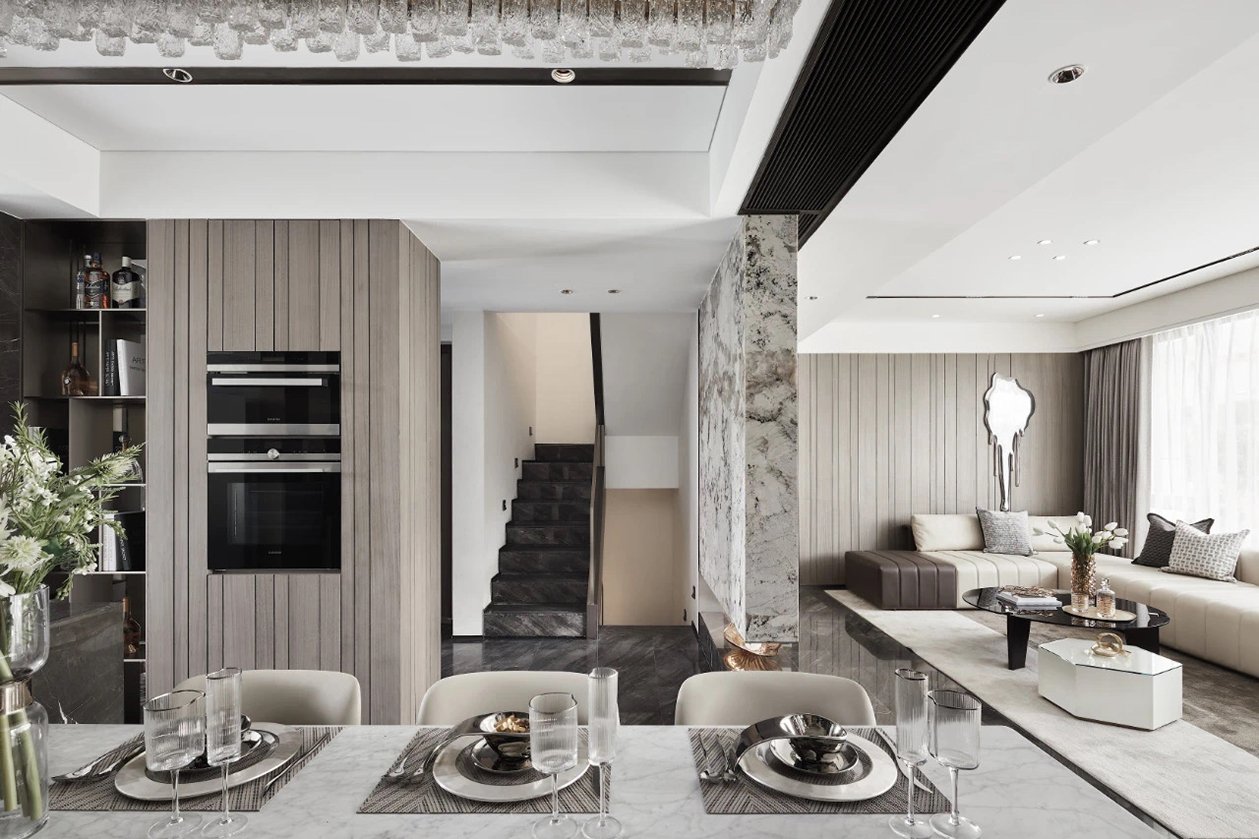 Open-plan dining and living space with a marble feature column, timber joinery and a staircase beyond